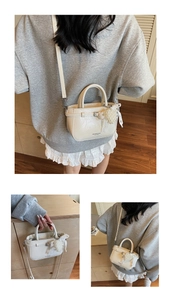 Close-up of cream Boston bag with metallic buckle and pearl flower charm detail