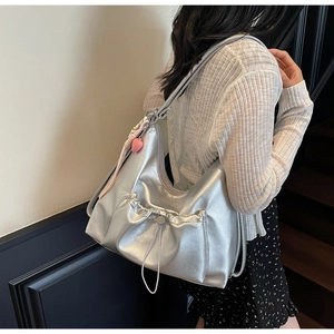 Detail of silver metallic tote bag featuring drawstring pleats and a pink heart charm