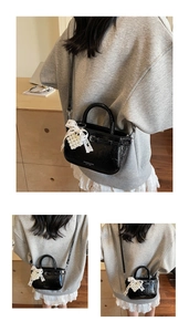Detail of a mini black glossy handbag with pearl heart charm and lace bow decor