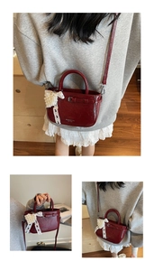 Detail of burgundy patent leather handbag featuring pearl heart charm and metal buckle