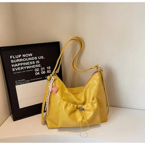Detail of yellow pleated tote bag featuring a front drawstring pocket and heart pendant