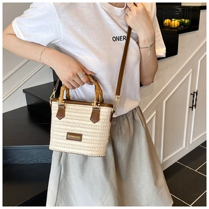 Detailed view of woven straw bucket bag with bamboo handles and brown leather trim