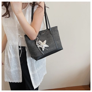 Detail of grey textured tote bag featuring a silver star charm and a leather fashion label