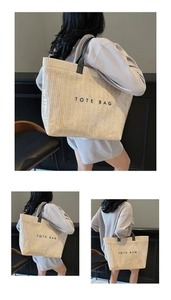 Detail shot of a large woven tote bag featuring black handles and TOTE BAG slogan print