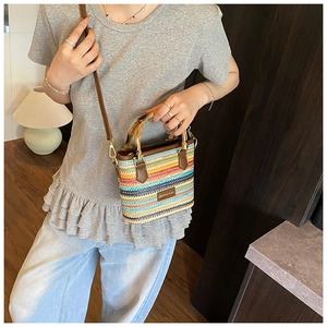 Close-up of bohemian multi-color woven straw bucket bag with natural bamboo handles