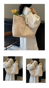 Detail view of woven straw tote bag with green TOTE BAG embroidery and leather handles