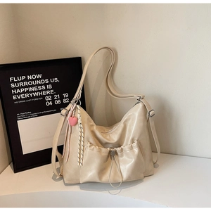 Detail of cream white pleated shoulder bag featuring a metal buckle pocket and heart charm