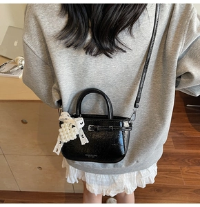 Detail view of black glossy handbag featuring lace bow and elegant pearl charm detail
