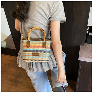 Detail of rainbow woven straw bucket bag featuring bamboo handle and leather strap