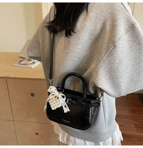 Detail of black glossy mini handbag with pearl heart charm and lace bow decoration