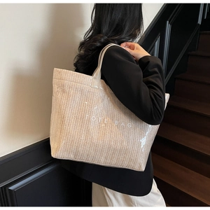Detail of a large woven tote bag with a transparent PVC outer shell worn by a model