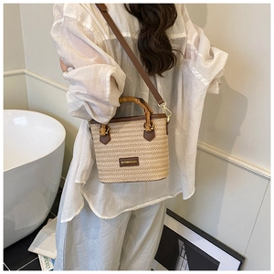 Detail of hand-woven straw bucket bag with bamboo handle and leather shoulder strap
