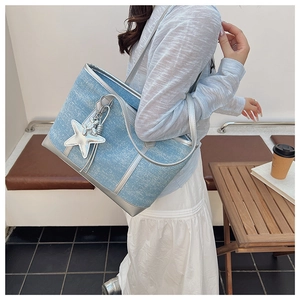 Close-up of light blue denim tote bag with silver leather trim and star charm detail