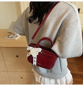 Lifestyle shot of a burgundy patent leather handbag with pearl heart and lace bow detail
