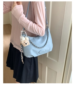 Detail of light blue tote bag with metallic chain, oval logo, and cute bear pendant