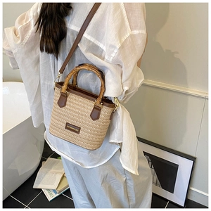 Detailed view of woven straw bucket bag with bamboo handle and brown leather straps