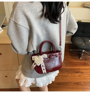 Detail of burgundy patent leather handbag with pearl heart pendant and lace bow