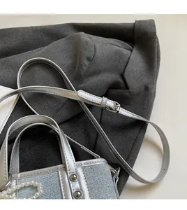 Detail der metallisch silbernen Beuteltasche mit verstellbarem Riemen und Perlenkette
