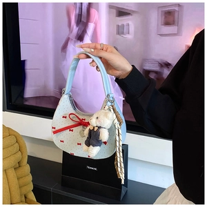 Détail du sac croissant bleu clair à motifs nœuds rouges avec breloque ours en peluche