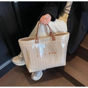 Detail of woven straw tote bag with clear PVC overlay and leather handles held by a model