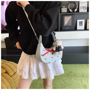 Détail du sac croissant bleu clair avec motifs nœuds rouges et un charm ours en peluche blanc