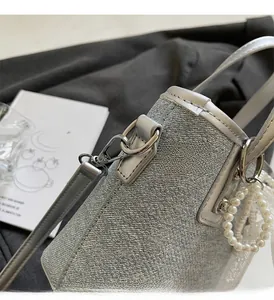 Detail einer grauen Denim-Eimertasche mit Metallhaken und Perlenspitzen-Anhänger
