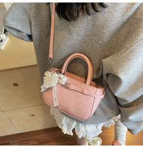 Pink mini crossbody bag featuring lace trim, pearl charm, and buckle detail shown on model