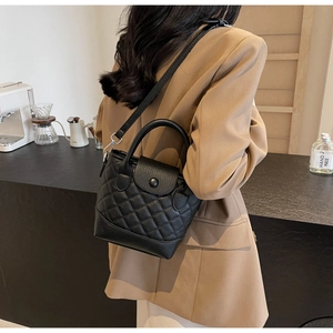 Detail of black quilted bucket bag featuring top handle and detachable leather crossbody strap