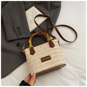 Close-up of woven straw bucket bag with bamboo handle and premium brown leather trim