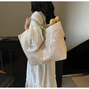 Detailed side view of large woven straw tote bag with TOTE BAG print and green handles