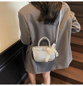 Detail of silver metallic tote bag with lace bow and pearl heart charm on a grey suit