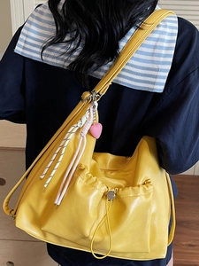 Fashionable yellow pleated tote bag with heart charms shown on a model's shoulder
