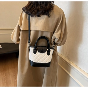 Rear view of a model in a trench coat with a quilted black and white bucket crossbody bag