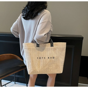 Close-up of beige woven tote bag with black text and handles in a modern lifestyle setting