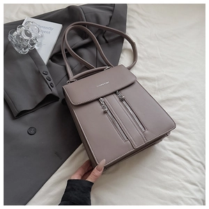 Détail d'un sac à dos en cuir taupe avec fermetures éclair argentées et lettrage