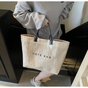 Detail of beige woven tote bag with V-shaped texture and black leather handles