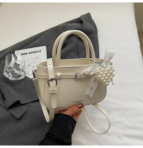 Detail of cream retro bag with pleated texture, silver buckle, and pearl heart pendant