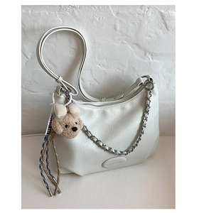 Detail of white tote bag with textured synthetic leather and silver chain strap with bear charm