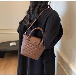 French style brown quilted leather bucket bag worn as a crossbody by a model