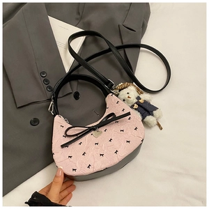 Détail de la sacoche rose gaufrée avec des nœuds noirs et un pendentif en forme de cœur
