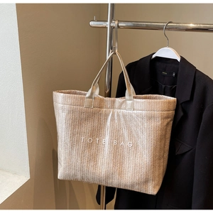 Detail of hand-woven straw tote bag with white TOTE BAG lettering and dual top handles