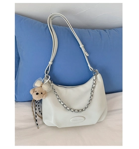 Close-up of white leather shoulder bag with silver chain, logo, and cute bear charm
