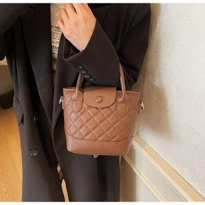 Detail of dark brown quilted leather bucket bag with top handles and pebbled texture