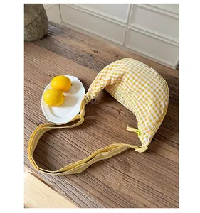 Detail of yellow checkered dumpling bag with adjustable striped strap on wooden surface