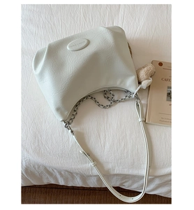 Detail of off-white lychee leather half-moon bag with silver chain and bear charm
