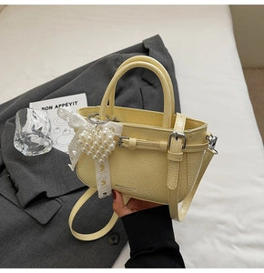 Detail of light yellow textured handbag with lace bow and pearl heart pendant