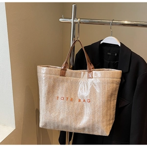 Detail of light beige woven tote bag with orange TOTE BAG text and brown leather handles