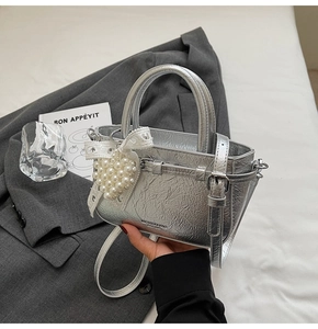 Detail of silver metallic handbag featuring lace bow and pearl heart charm accessory
