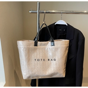 Detail of light brown woven tote bag featuring black handles and TOTE BAG lettering
