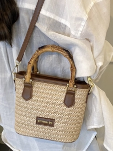 Handwoven straw bucket bag with bamboo handle and leather trim on a white shirt model